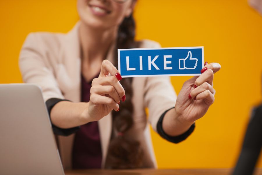 A woman holds up a blue sign that says "LIKE" with a thumbs-up icon.