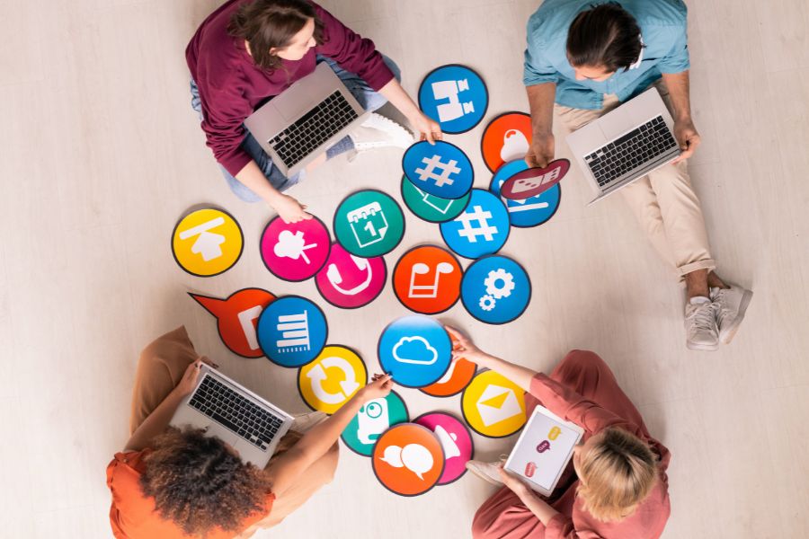 An overhead view of four people sitting on the floor, working on laptops around a collection of large social media icons.