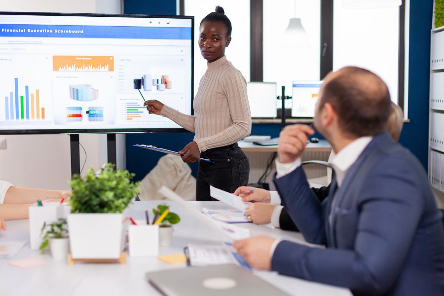 A woman gives a presentation with charts and graphs to her colleagues in a meeting room.