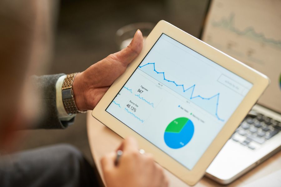 A person in a suit reviews business analytics charts and graphs on a tablet.