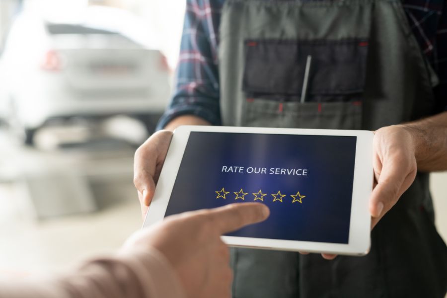 An auto mechanic holds a tablet that says "RATE OUR SERVICE," and a customer is about to tap one of the five stars to leave a rating.