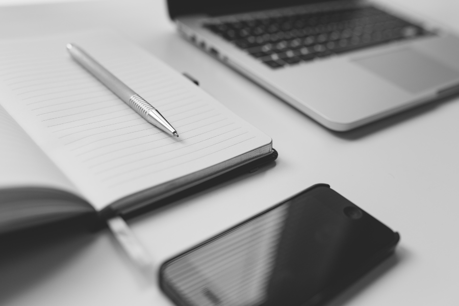 Black and white image of a notebook, a pen resting on it, and a smartphone beside them.